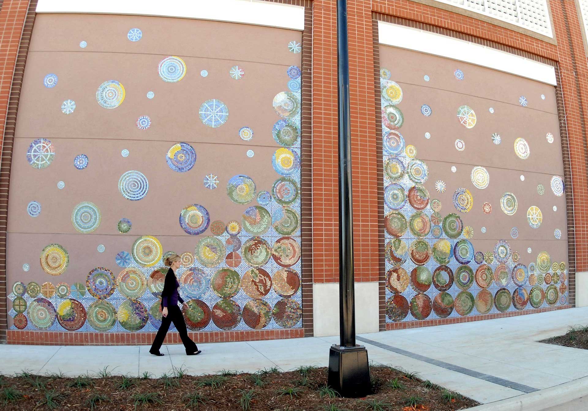 Woman walking on sidewalk past 3 story colorful mosaic tile wall